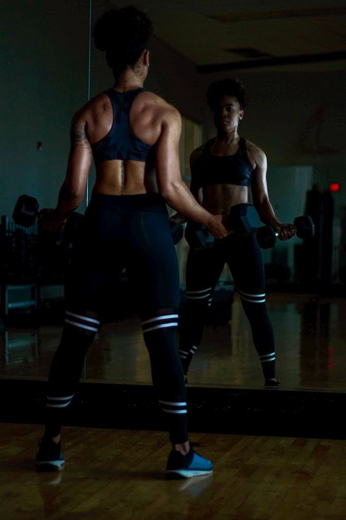 A determined woman lifting weights in a gym while looking at her reflection in a mirror.
